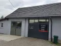 Budynek warsztatu samochodowego z szarym dachem i drzwiami garażowymi z logo "maxserwis".