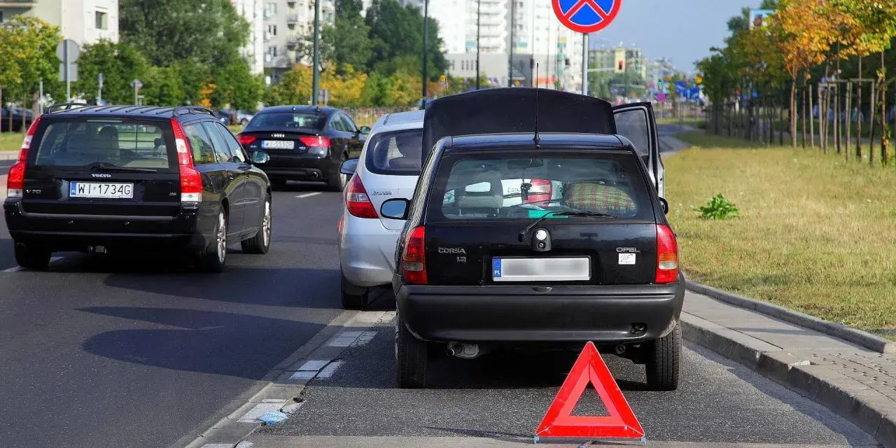 Czarny Opel z otwartą klapą bagażnika i trójkątem ostrzegawczym na autostradzie.