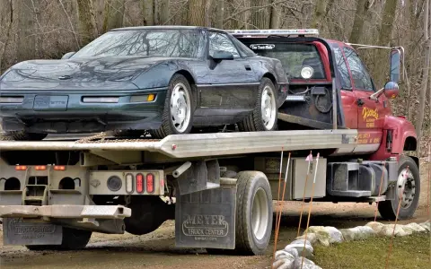 Czerwona laweta z zielonym Chevroletem Corvette na platformie.