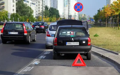 Czarny Opel z otwartą klapą bagażnika i trójkątem ostrzegawczym na autostradzie.