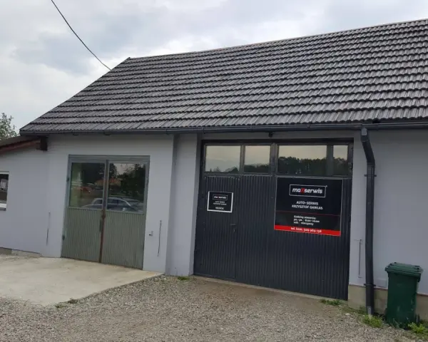 Budynek warsztatu samochodowego z szarym dachem i drzwiami garażowymi z logo "maxserwis".