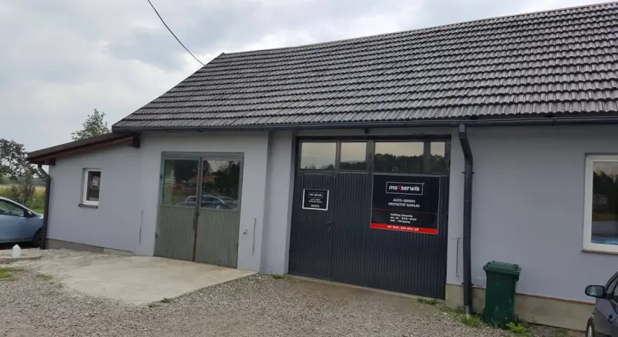 Budynek warsztatu samochodowego z szarym dachem i drzwiami garażowymi z logo "maxserwis".