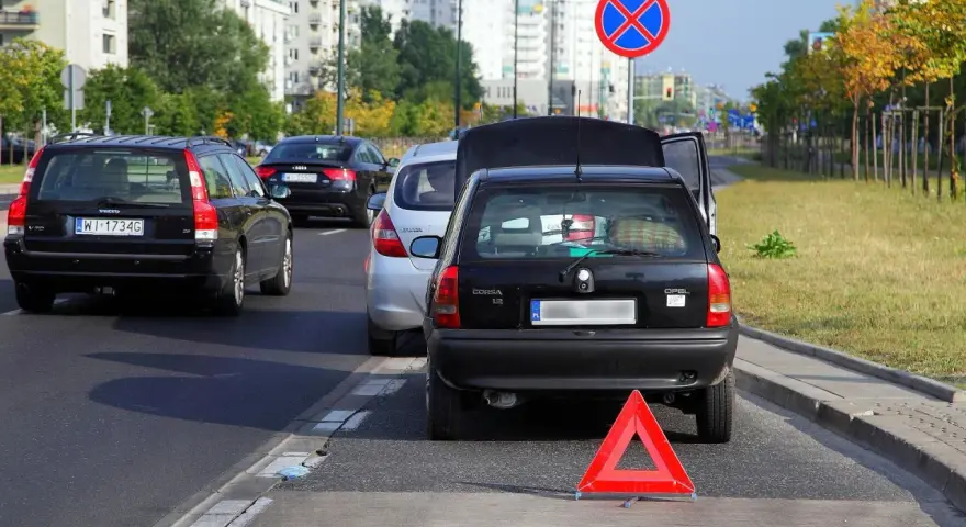 Czarny Opel z otwartą klapą bagażnika i trójkątem ostrzegawczym na autostradzie.